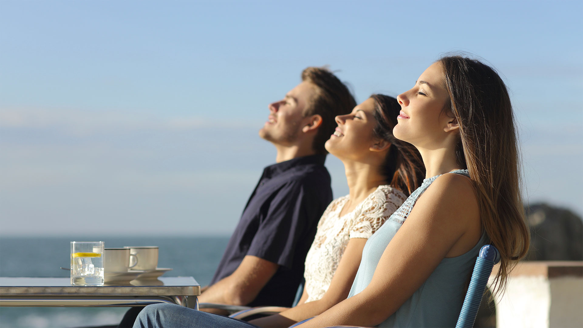 Dvě ženy a jeden muž si užívají klidný víkendový moment s výhledem na moře.