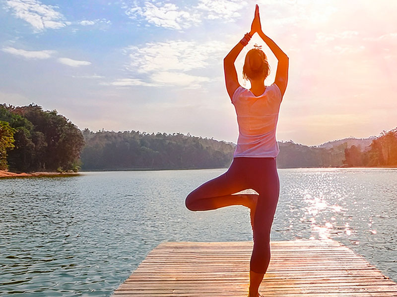 Žena cvičí jógu na dřevěném molu u jezera při východu slunce.